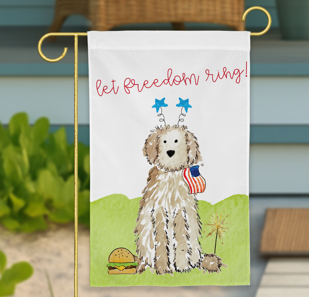 Decorative garden flag with a dog holding an American flag and text 'let freedom ring!' on a blurred outdoor background. fourth of july garden flag, doodle garden flag, patriotic dog garden flag, goldendoodle july 4th flag, labradoodle american flag, doodle patriotic yard flag, 4th of july dog flag, independence day dog decor, red white and blue garden flag, summer dog yard flag, sparkler dog flag, doodle dog decorations, customizable doodle flag, dog lover patriotic decor
