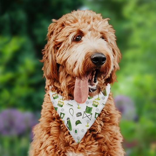 A brown dog wearing a golf dog bandana with a green and yellow golf-themed pattern. Pattern includes pimento cheese sandwiches, egg salad sandwiches, patron tournament chairs, green caps, golf balls, tournament cups, cameras and more!