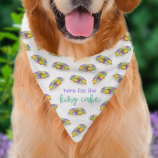 Mardi Gras Dog Bandana, Dog wearing a bandana with king cake pattern and text 'here for the king cake' against a blurred green and purple background.